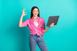 © deagreez - Photo portrait of pretty teen girl hold netbook wink show okey wear trendy pink outfit isolated on aquamarine color background