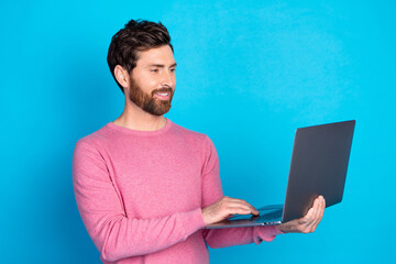 Wall Mural - Confident young man holding laptop, wearing pink sweater, isolated against a vibrant blue background, suitable for tech and lifestyle concepts