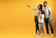 © Prostock-studio - Wow offer. Full body length portrait of excited black family looking and pointing aside at copy space on yellow background, demonstrating free place for your advert, panorama, banner