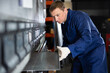 © JackF - Experienced middle-aged man in blue workwear and protective gloves placing metal sheet on bending machine in metalworking workshop..