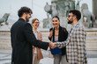 © qunica.com - Group of business people meeting and shaking hands outdoors in a city. They are smiling and discussing ideas, symbolizing cooperation and teamwork in a collaborative urban environment.