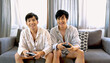 © aFotostock - Happy gay couple enjoy playing game together sitting sofa at home living room lifestyle. Friendship gamer men use joystick playing have fun happy time. Two best friends LGBTQ relation partner home