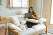 © Stella 16 - A woman is sitting on a couch with a tablet in her hand. She is smiling and she is enjoying her time.