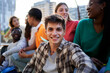 © Gigi Delgado - Cheerful portrait of a young caucasian male student looking at camera while sitting outside university gathering with friends.