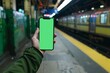© AHNH2 - Hand Holding Smartphone with Green Screen at Urban Subway Station, Displaying Technology Use in Public Transport Settings, Ideal for Advertisements and Digital Marketing