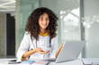 © Liubomir - Smiling female doctor engaging in online consultation, showcasing telemedicine advancement. Confident healthcare professional utilizing laptop for telehealth in modern medical office.