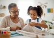 © Running opossum - Grandmother and granddaughter sewing together at home, sharing a special moment and learning a new skill