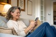 © Yauhen - Relaxed mature old 60s woman, older middle aged female customer holding smartphone using mobile app, texting message, search ecommerce offers on cell phone technology device sitting on couch at home