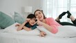 © Summit Art Creations - Happy asian daughter and smart mom lie on bed while looking at camera. Energetic family spend time and prepare to sleep together. Cute girl and mom smile to camera show love and affection. Pedagogy.