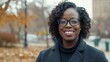 © 69 - Professional African American Woman Smiling Outdoors in Fall Season, Wearing Black Turtleneck and Gray Coat with Urban Background and Autumn Leaves