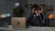 © kinomaster - Adult business man manager sitting at desk working on laptop in office in evening, typing on computer doing research, bored expression.