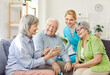 © Studio Romantic - Female pensioner showing something funny on mobile phone to senior group of people and friendly nurse. Elderly men and women spending time together, using internet during leisure in nursing home.
