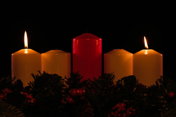 four white advent candles in a row where two are lit, with a red unlit Christ candle in the center, and garland below. 