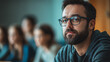 © Chanyapat - focused man with glasses listens attentively in modern classroom setting, surrounded by fellow students. His expression reflects engagement and curiosity