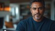 © by - A contemplative man with salt-and-pepper hair gazes thoughtfully at the camera in a cozy setting.