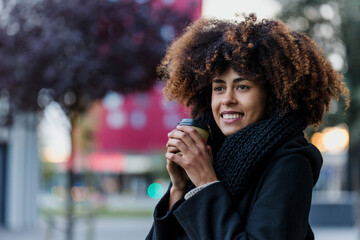 Wall Mural - young African American business woman holding coffee cup in city of Spain Europe, Hispanic financial and caribbean people with skyscraper background