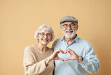 Smiling elderly couple joyfully making a heart shape with their hands, symbolizing love and companionship. This image captures the warmth and happiness in their enduring relationship.