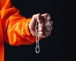 © Arnon  Parnnao - Prisoner offense fairness. A person holds a chain in hand, wearing an orange jacket against a dark background.