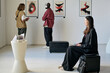 © AnnaStills - People of different backgrounds enjoying an art gallery with abstract paintings. Artwork displayed on white walls while individuals observe and interact in a serene atmosphere