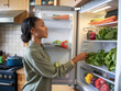 © Leonardo - Una mujer negra en la cocina, revisando el refrigerador en busca de verduras frescas