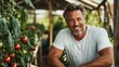 ©  Shomixer - A smiling man in a white t-shirt stands confidently among ripe tomatoes and green foliage in a greenhouse, reflecting agricultural success and tranquility.