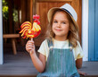 © Robert - A cheerful girl in denim overalls clutches a lollipop, embodying the joy and simplicity of childhood.