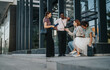 © qunica.com - A group of young business people having an informal meeting outside a modern office building. They are engaged in a lively discussion, exchanging ideas and collaborating on their project.