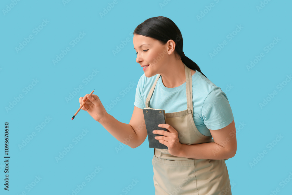 Beautiful young waitress with notebook on blue background