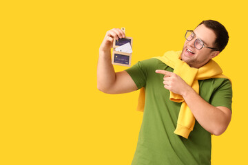 Wall Mural - Young happy man in eyeglasses holding wallet with credit cards on yellow background