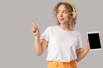 Canvas Print - Young woman in headphones with blank tablet computer pointing at something on light background