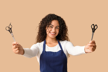 Wall Mural - Beautiful young happy African-American hairdresser with scissors on beige background