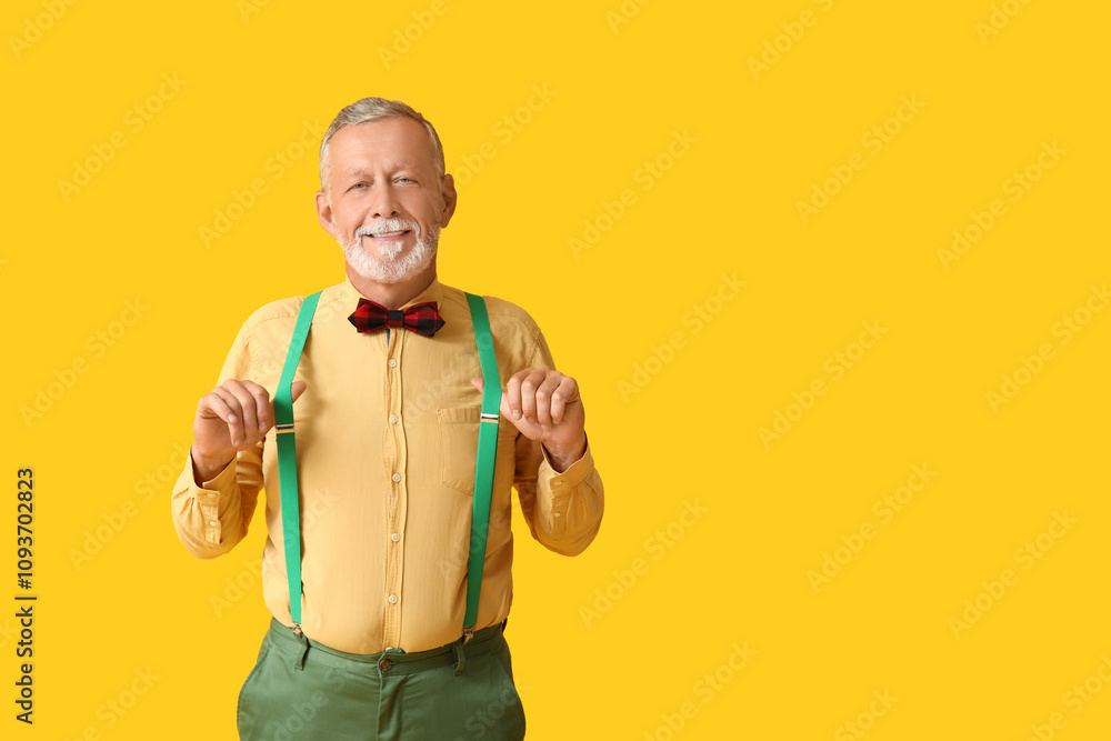 Handsome happy mature man with stylish bow tie on yellow background