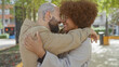 © Krakenimages.com - Interracial couple embracing lovingly in a sunny urban park, depicting joy and diversity.