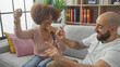© Krakenimages.com - A joyful interracial couple enjoy singing with a remote control as a microphone in a cozy living room setting.