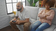 © Krakenimages.com - An interracial couple in a living room, man playing video games and woman upset, depicting relationship issues or leisure time conflicts.