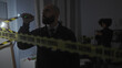 © Krakenimages.com - A man and woman investigate a dimly lit indoor crime scene with caution tape and evidence.