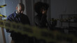 © Krakenimages.com - A man and a woman, appearing as detectives, investigate an indoor crime scene with caution tape.