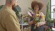 © Krakenimages.com - A woman florist presents flowers to a man in an indoor flower shop surrounded by various plants.