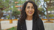 © Krakenimages.com - Smiling middle-aged hispanic woman with long brunette hair in a park setting with blurred urban background