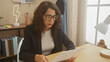 © Krakenimages.com - Mature woman reads document at home office with glasses and blazer, interior decor visible.