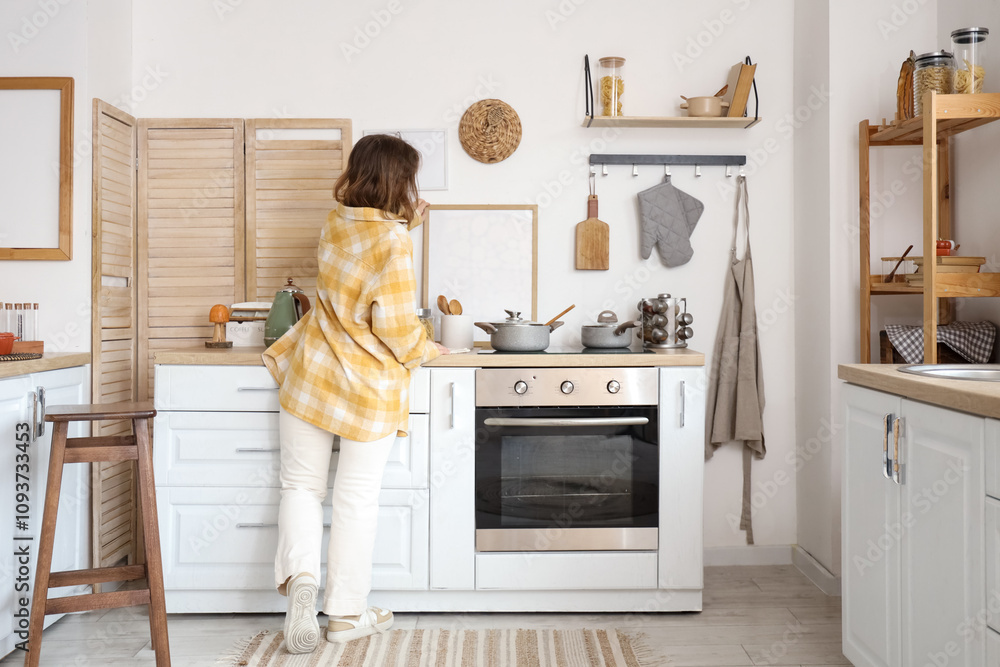 Young woman near counters in kitchen on autumn day, back view