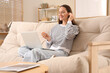 © Pixel-Shot - Young woman with laptop putting ear plugs on sofa at home