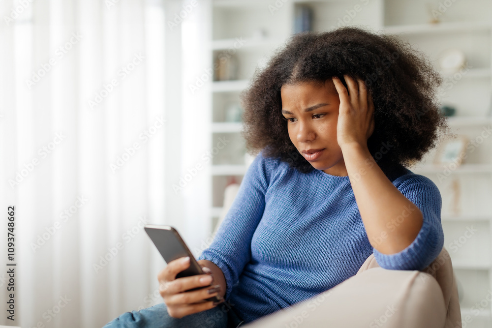 Concerned young black woman looking at smartphone screen and touching ...