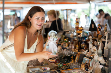 Wall Mural - Satisfied interested young woman choosing interesting antique things at traditional flea market