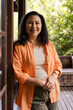 © Wavebreak Media - Smiling senior woman in orange shirt standing on porch, enjoying sunny day