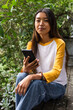 © Wavebreak Media - Sitting outdoors, asian female teenager holding smartphone and appreciating nature and technology