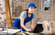 © JackF - Young woman builder using laptop while standing inside construction site.