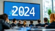© Thitiwadee - A group of professionals watches a presentation featuring '2024' on a large screen, set in a modern conference room.