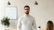© pattaphorn - A man with glasses stands confidently in a bright office space, wearing a light sweater, with plants and a whiteboard in the background.