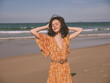 © SHOTPRIME STUDIO - Woman in orange dress standing on beach with hands on head in contemplation and relaxation
